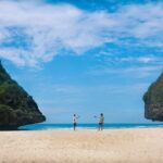 Spiaggia nascosta con sabbia dorata e acque cristalline, circondata da scogli e vegetazione lussureggiante.
